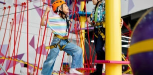 two children in helmets climb on zip line